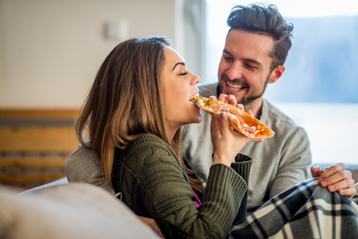 Young couple eating pizza in bed